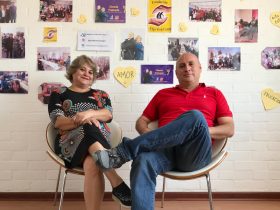 Foto de personas sentadas en una silla, con fotos a sus espaldas de gente sonriendo